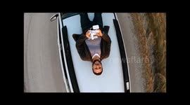 Man films himself from above while he lies on top of a moving car