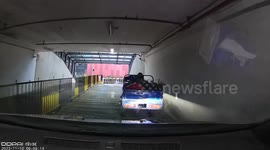 Car narrowly escapes collision with three-wheeler sliding down slope in underground garage
