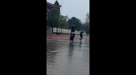 Three students fit themselves under single umbrella during rain