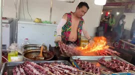 A street chef demonstrates his skills in grilling octopus on a skewer with a rising flame, surprising many tourists