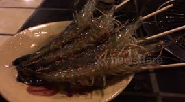 Live prawns wriggle on skewers at a Saigon restaurant