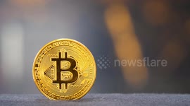 A physical Bitcoin coin in foreground pulled focus to a live feed digital display showing Bitcoin being bought using fiat currency around the world ahead of the BTC Halving.