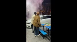 Bystanders use fire extinguisher to control flames on overheating car