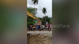 Stranded locals ride excavator bucket to cross broken bridge after storm
