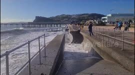Boy takes a chance in hanging on to rail in severe waves in Teignmouth sea front.