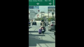 Tourist drags cabin bag behind motorcycle on busy Thai motorway