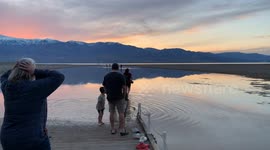 People frolic in Manly Lake, an unusual lake that has formed in Death Valley's Badwater Basin (from extreme rainfall). People have come from all over to to paddleboard and wade in this salty lake as the sun sets over the desert mountains, reflecte