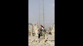 Two men raising the national flag of Jordan in Jerash Ruins. Jerash is an ancient city located in Jordan that dates back to the Greco-Roman period. It is one of the best-preserved Roman cities in the world