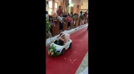 Baby bridesmaid cruises down wedding aisle in toy car