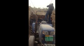 Man drives tractor backwards with one foot on steering wheel