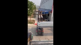 Two forklift drivers coordinate professionally to move large iron pipes off the truck and into the warehouse