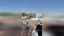 College students sit in perfect row behind pillar's shade to keep cool on hot day
