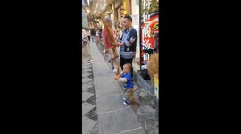 Toddler mimics performer playing traditional Chinese instrument