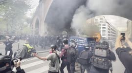 Police charge at protesters through clouds of teargas near a burning vehicle in Paris on May Day 2024