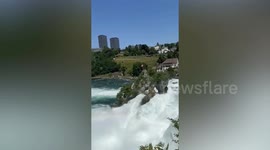 Tourists enjoy boating along large plain waterfall in Switzerland
