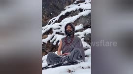Indian guru sitting in snow while meditating on mountain