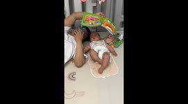 Playful baby sneaks peeks at cellphone screen instead of reading with dad in China