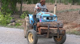 A farmer transports timber on his tractor on a rural farm in Thailand.