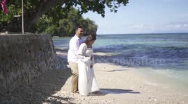 Sudden wave drenches couple posing on beach for wedding pictures