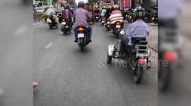 A man with two amputated arms drives a three-wheeled vehicle with his feet, weaving through the crowded crowd of people in Vietnam