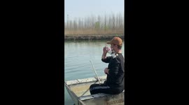 Chinese man fishing while feeding kitten on his shoulder