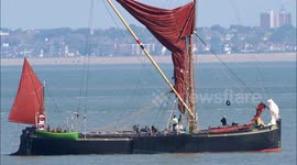 Moment paddleboarder stops by a Thames sailing barge for a quick chat off Kent, UK
