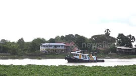 A barge being towed on a river, with a sea of moving green plants floating by, at Bang Pa In, Thailand