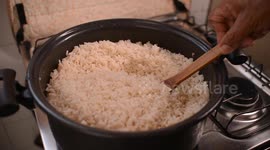 White rice cooking in the pan. White rice being stirred with a wooden spoon in the pan