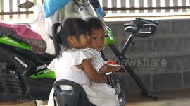 Two little kids take an uncomfortable trip on a tricycle, a boy and a girl, both are 2 years old.