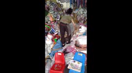 Elderly shopkeeper climbs over piles of rubbish in messy store
