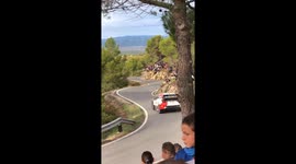 rally car drifting on a windy road past a big crowd