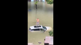 Drunk man stands on top of damaged car soaking in flood water