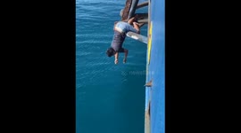 Person catches fish while perched on ship's side in Indonesia