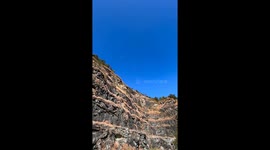 Slackliner balances above rocks while dirt bikers navigate below