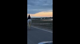 Girl rides white horse as lightning streaks across sky behind her