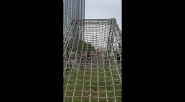 Woman tumbles on netting while climbing obstacle course and hitting her friend