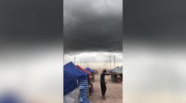 Vendors secure tents with ropes in market as dark cloud hovers with storm