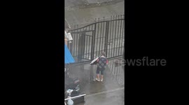 Elderly man struggles to pass through metal gate relentlessly spinning in Typhoon Bebinca winds