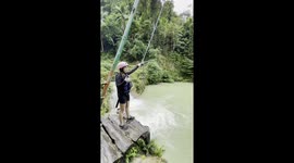 Tourist prays and swings on rope over river