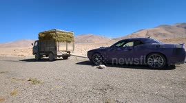 An old Soviet farm truck towing a modern American V8 muscle car in the Tajikistan mountains