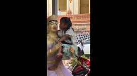 Girl chills in the arms of Buddhist deity statue at local temple