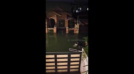 Neighbours use plastic chairs to cross flood outside their home