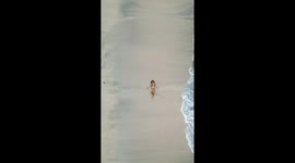 Wave hits bikini-wearing beachgoer as she poses on sand