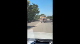 Farm equipment bounces along road while being pulled by tanker