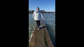Couple get soaked by incoming tide as they walk along tide wall in UK