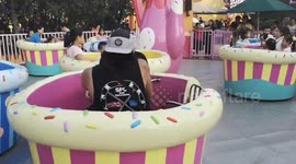 Grown men have fun playing on spinning teacups at fairground