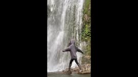 Girl topples into pool while posing in front of waterfall