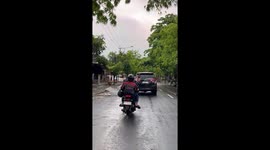 Guy sits uniquely on motorcycle with legs pointing upward in Ngawi, Indonesia