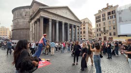 A street performer dressed as a flying lamp genie attracts laughter from passers-by in a Piazza della Rotonda packed with tourists, with the Pantheon in the background, in Rome.