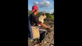 Cyclist rides bike with his pet dog in his lap